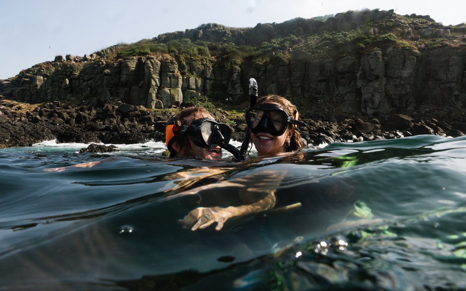 Two snorkellers in the water in front of a rocky headland